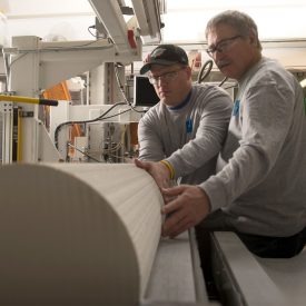 Two workers maneuver solid, log-size ceramic material on machinery