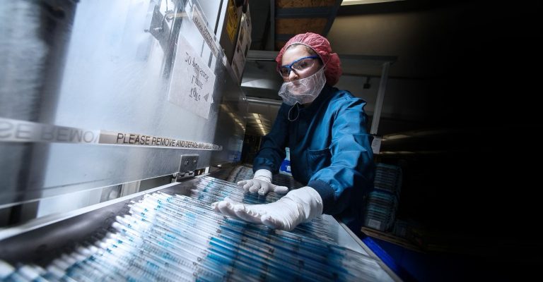 Woman working on production line in blue overalls, red hair net and safety glasses